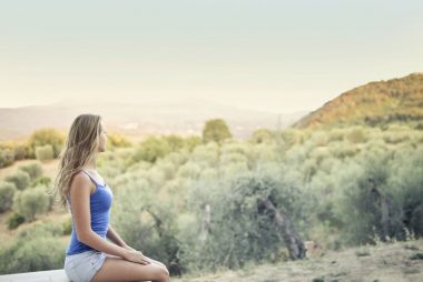 A woman in casual attire sits peacefully, enjoying a scenic outdoor view of nature.